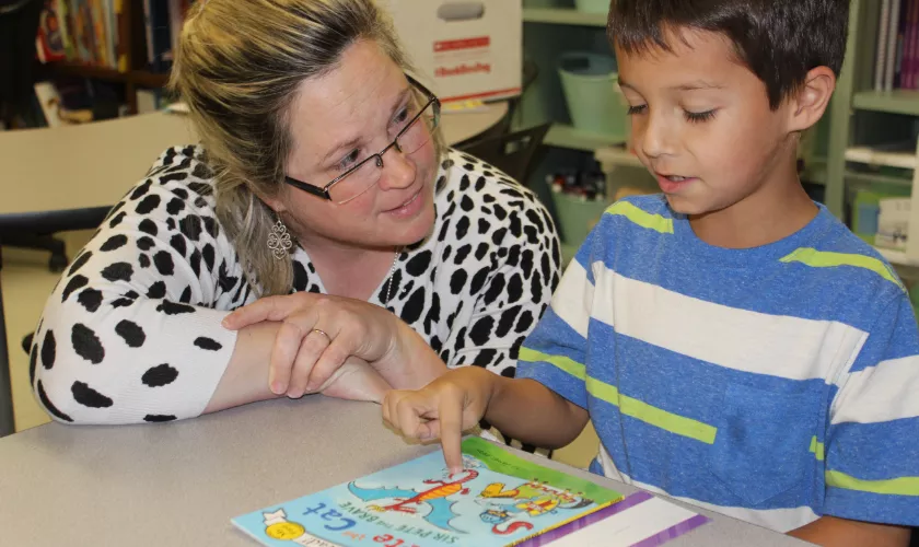 teacher working with a student in class while the student reads them a passage